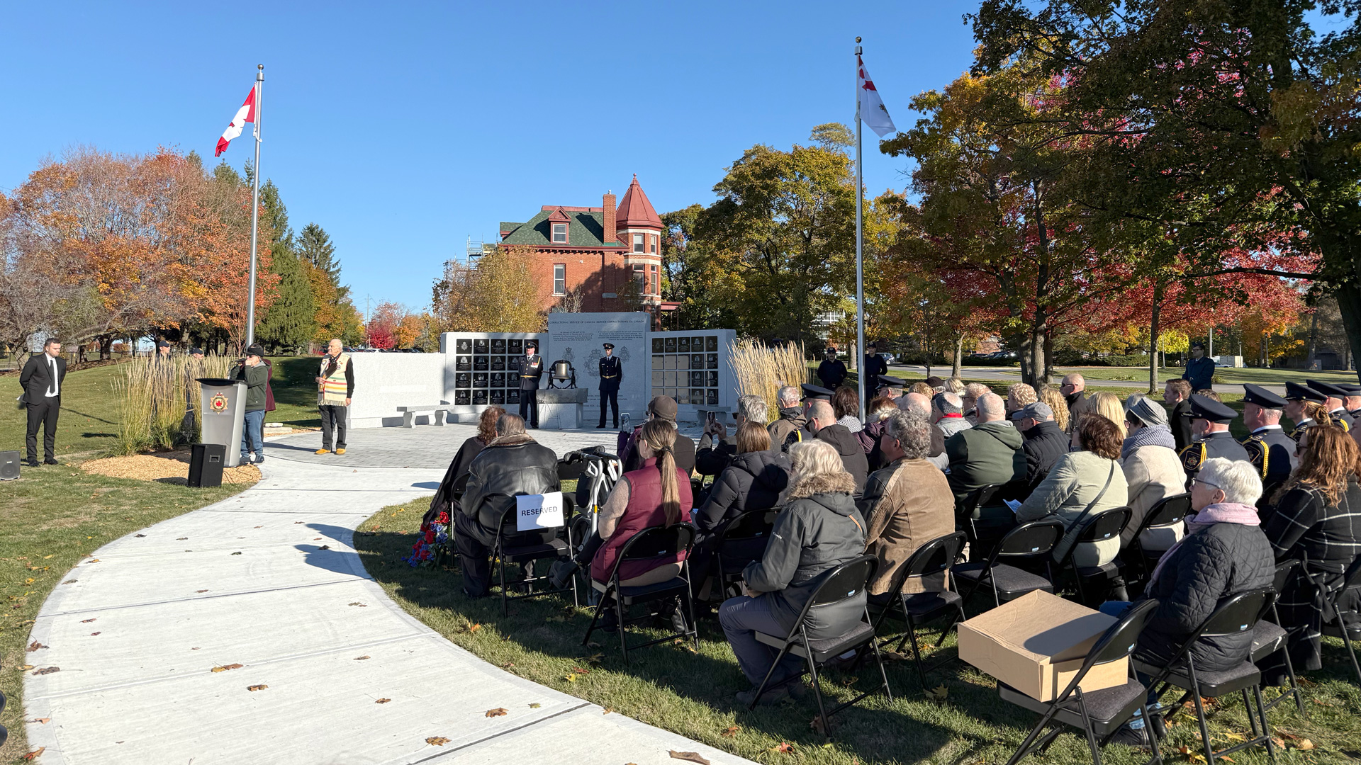 Group of people sitting in front of person speaking who is dedicating the CSC Memorial